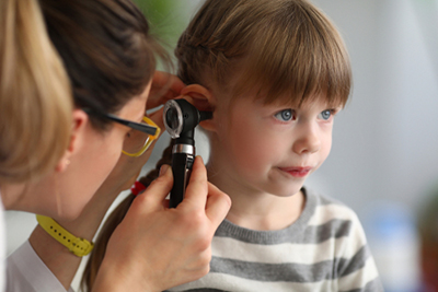 Pediatric ENT specialist examining a child’s ear with otoscope